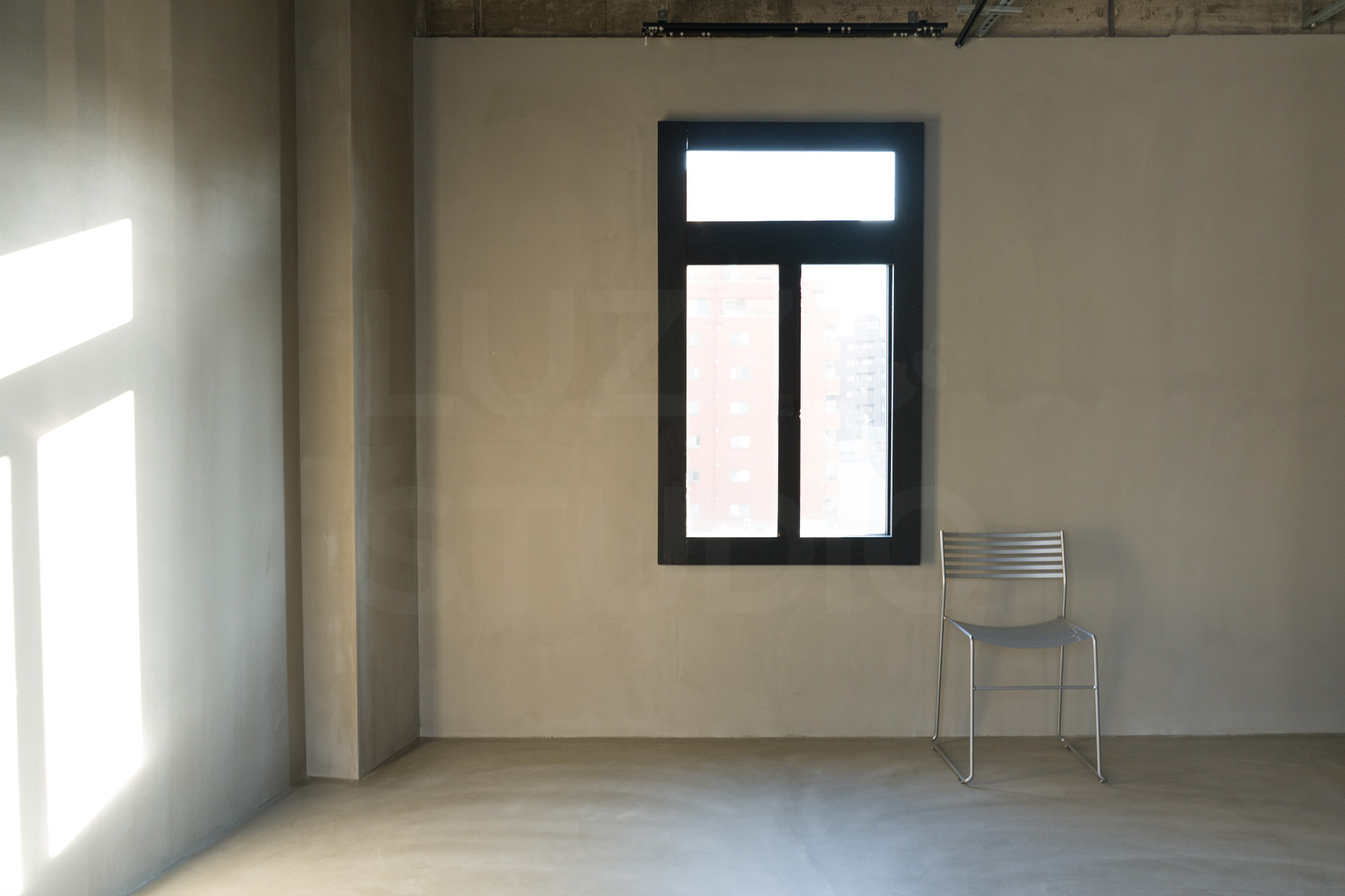 光のラインが壁面に落ちるグレーの撮影エリア。窓際にシルバーのメタルチェアを配置した、シンプルで静謐な大阪のスタジオ内装