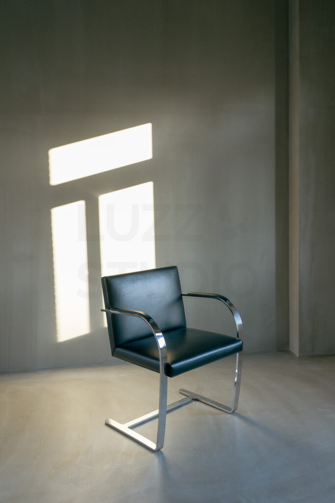 光のラインが壁面に落ちるグレーの撮影エリア。窓際にシルバーのメタルチェアを配置した、シンプルで静謐な大阪のスタジオ内装