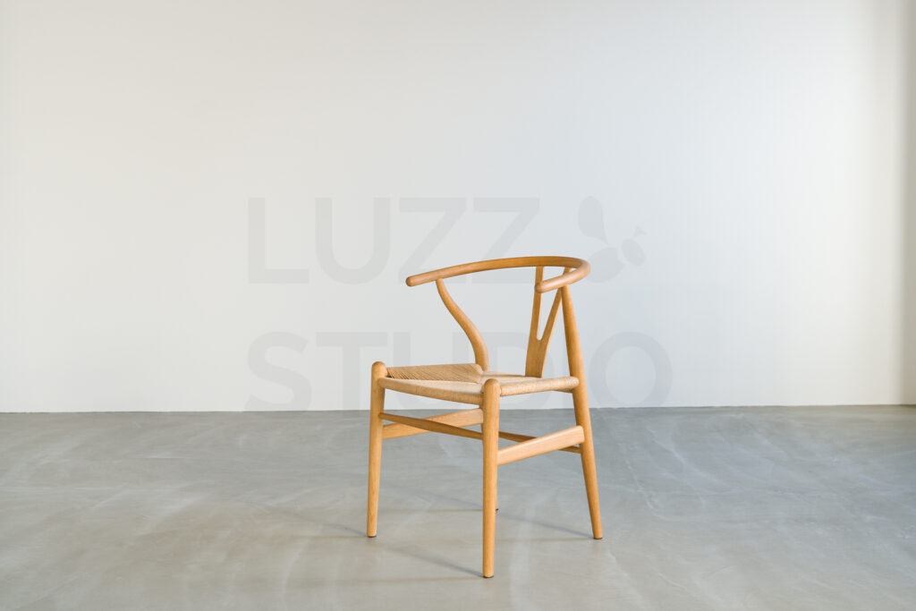 真っ白な壁とグレーのコンクリート床の境界に置かれた、ナチュラルな木製アームチェア。余白を大きく取った構図の大阪のスタジオ内装