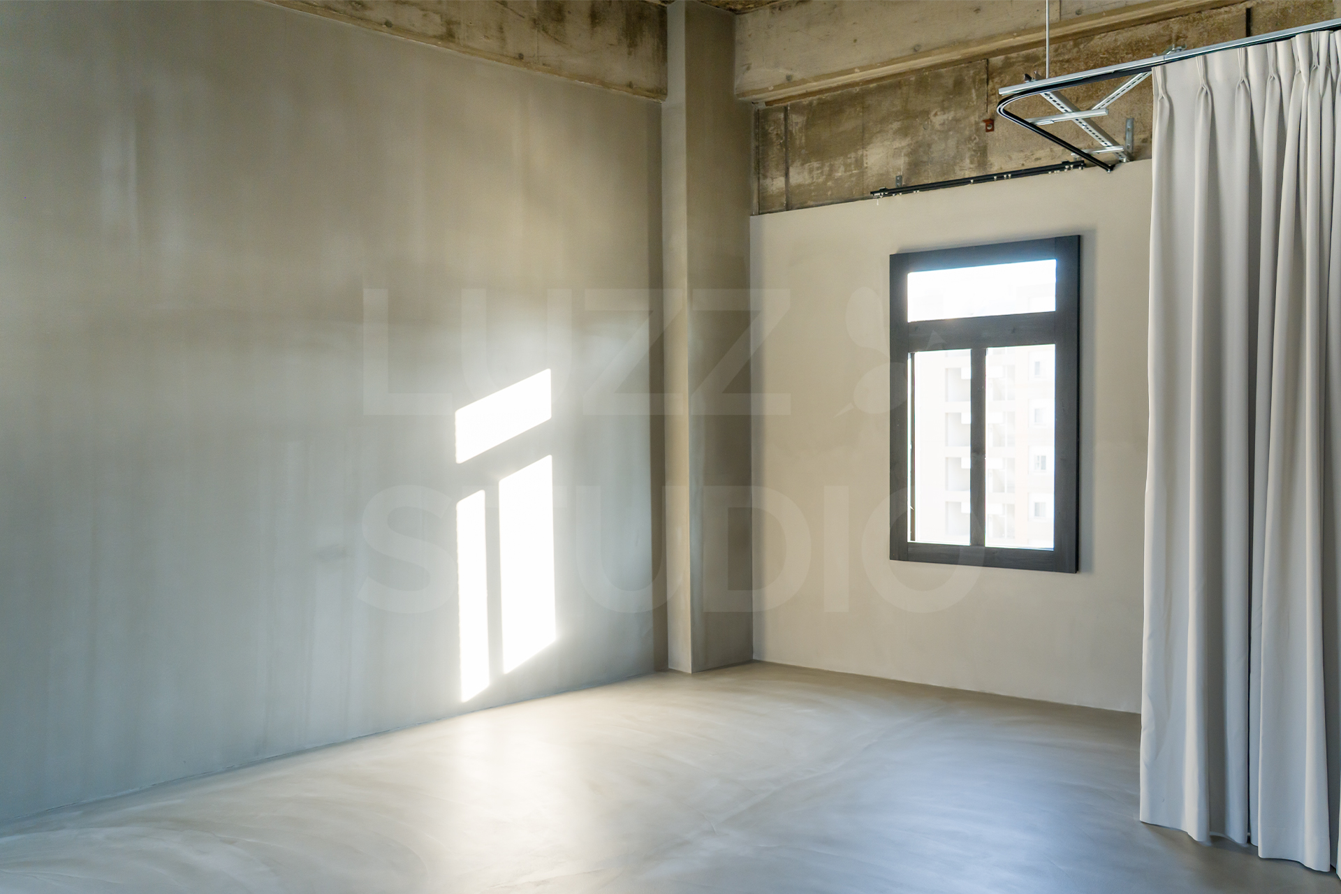 大阪のレンタル撮影スタジオ、グレーのモルタル壁面に差し込む鮮やかな自然光。光と影のコントラストを活かしたドラマチックな背景の撮影スペース