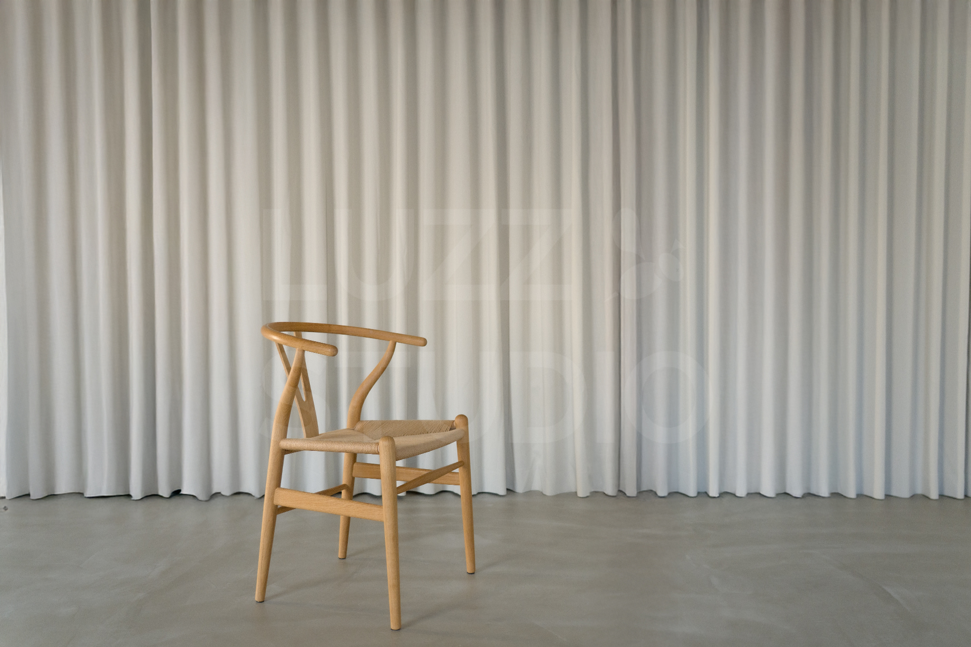 プリーツ状の白いカーテンを背景に、モルタル調の床に置かれた1脚の木製デザイナーズチェア。シンプルで開放的な大阪のスタジオ内装と自然なライティング
