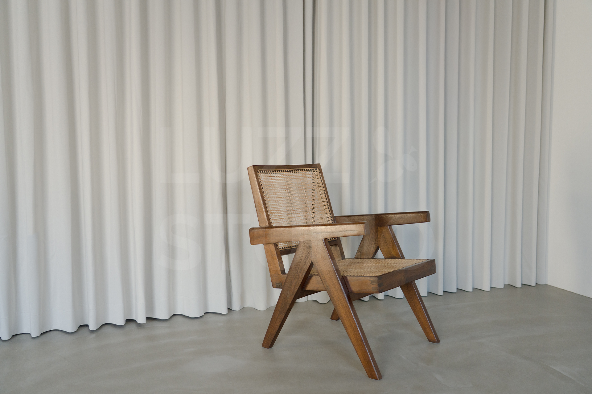 プリーツの入った白いカーテンの前に置かれた、ラタン編みのアンティーク調チェア。グレーのコンクリートフロアが広がる、モダンで静謐な大阪のスタジオ内装