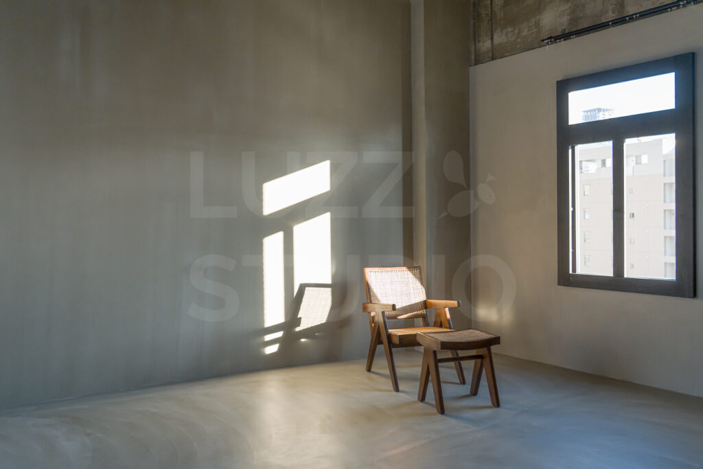 大阪のレンタル撮影スタジオ。グレーのモルタル壁に差し込む印象的な自然光と、ピエール・ジャンヌレのラウンジチェア。光と影のコントラストを活かした洗練された撮影シーン