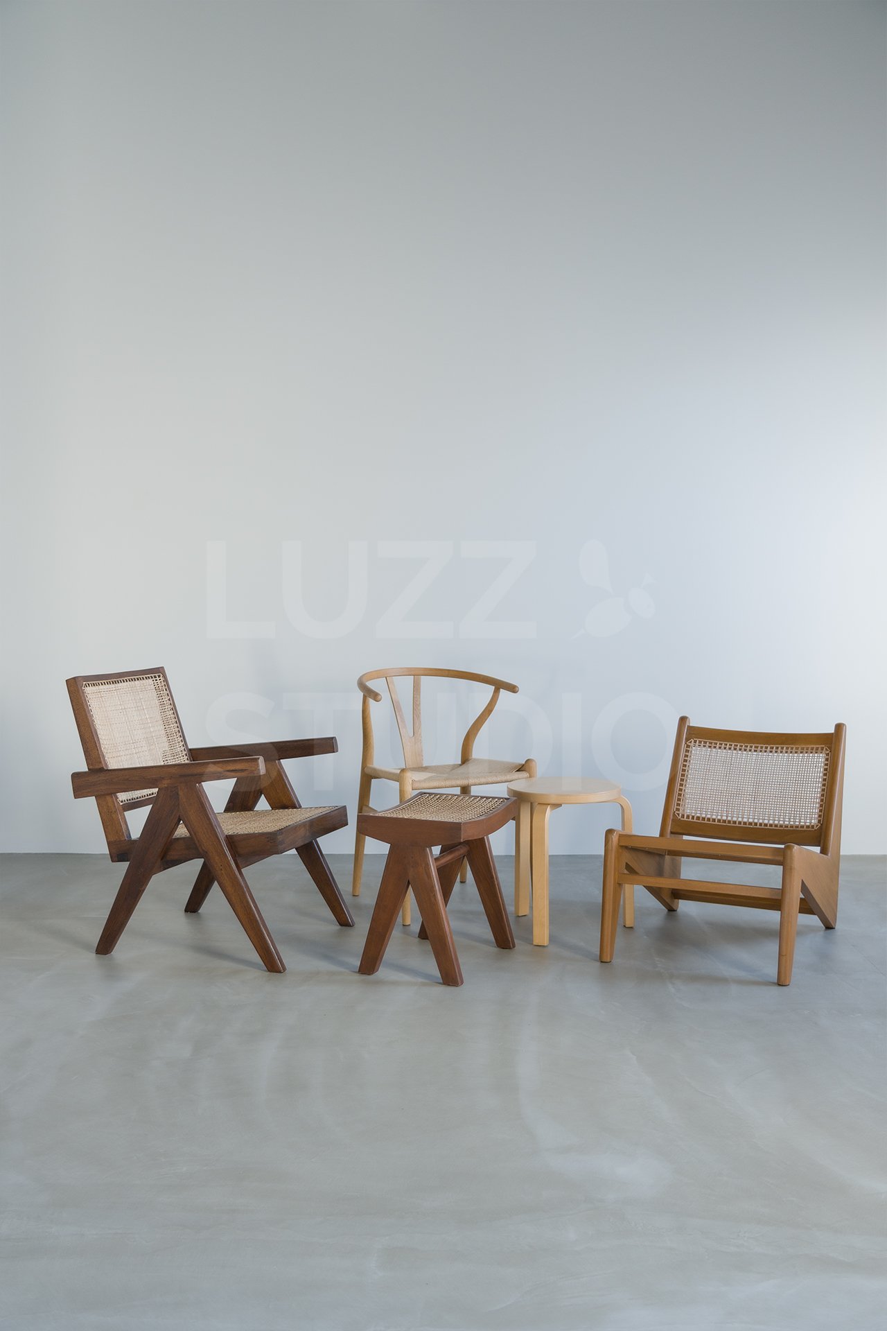 ラズスタジオのモルタルグレー床、白壁背景の前に常設家具のPierre Jeanneret、Yチェア、カンガルーチェアなどのデザイナーズ家具のある室内写真