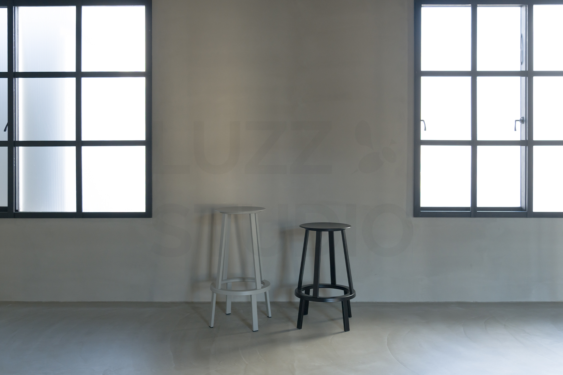 大阪のレンタル撮影スタジオ。2面の格子窓から自然光が差し込むグレーモルタル壁の撮影エリア。モノトーンのハイスツールを配したモダンで無機質な空間