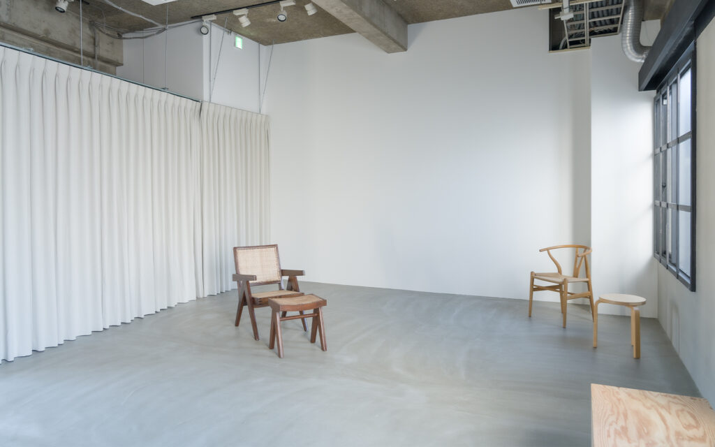 大阪のレンタル撮影スタジオ。白壁とコンクリート床の空間にピエール・ジャンヌレやYチェアが並ぶ自然光スタジオの内観