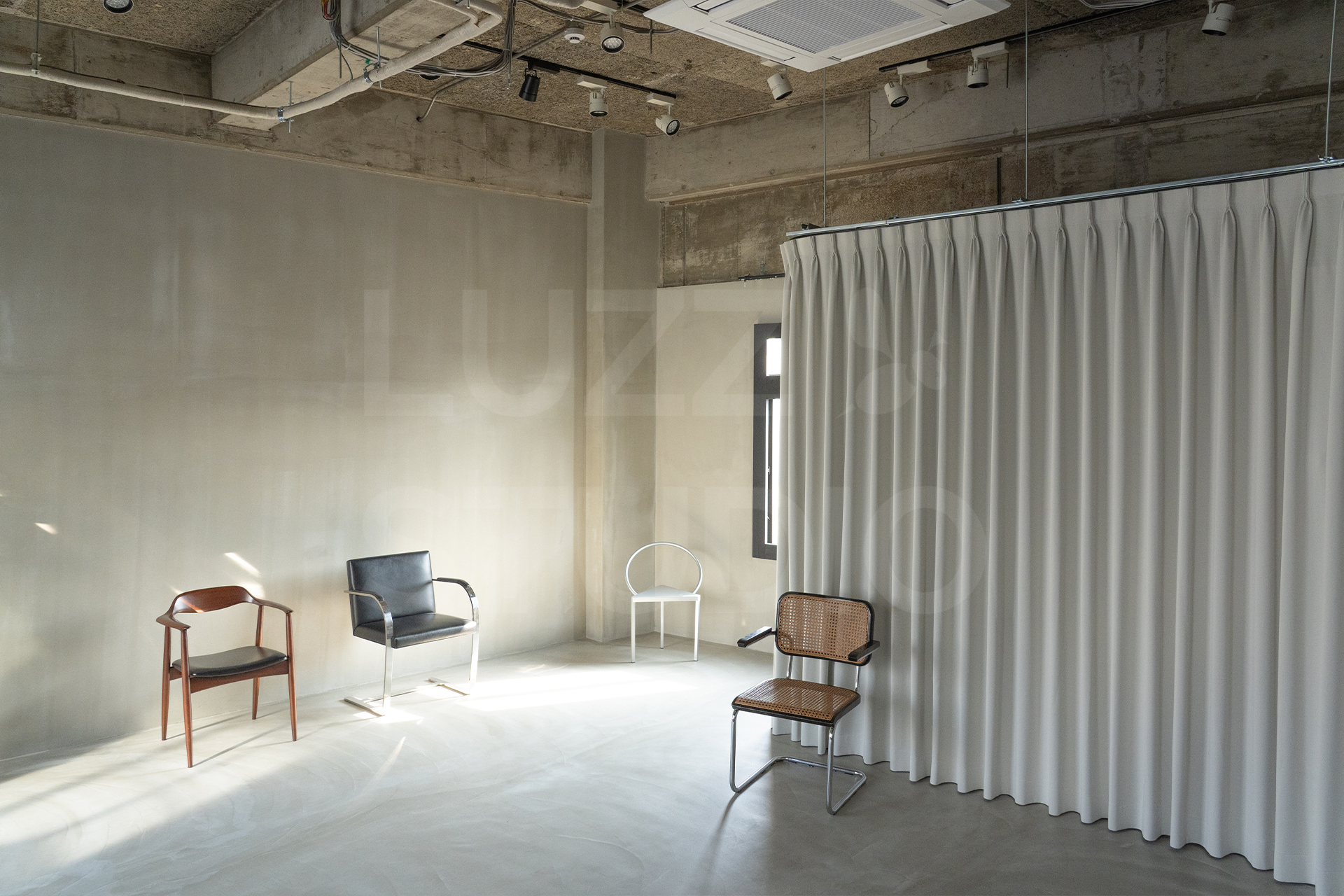 ラズスタジオのモルタルグレー床の室内写真。グレー壁とカーテン背景を収めた写真で、常設家具を用いた広さのわかる写真