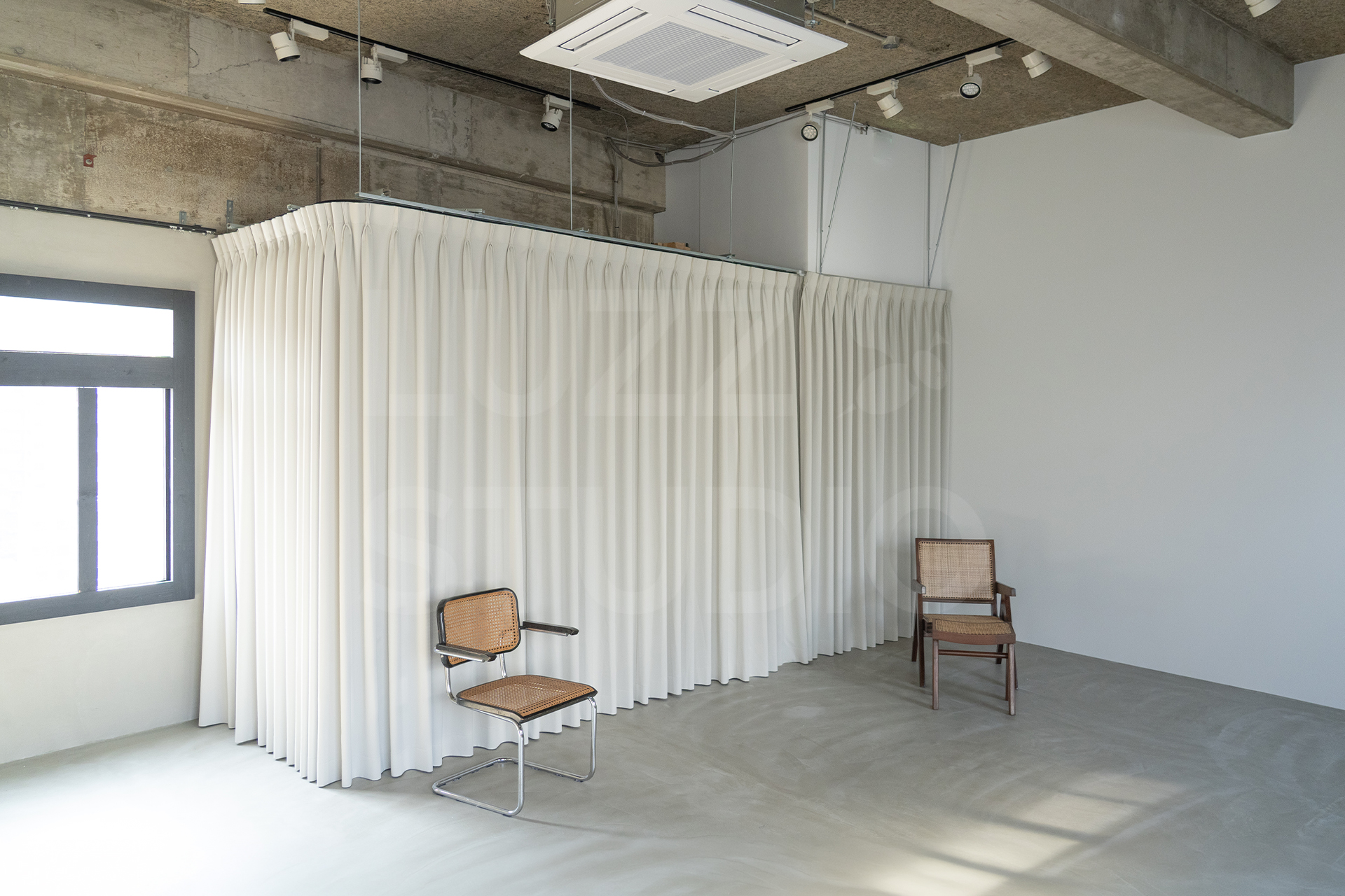 ラズスタジオのモルタルグレー床の室内写真。カーテン背景を収めた写真で、常設家具を用いた広さのわかる写真