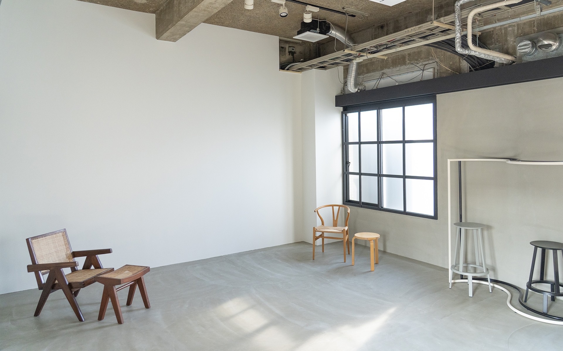 大阪のレンタル撮影スタジオ「LUZZ STUDIO」のモルタルグレー床 × 白壁 × グレー壁空間の写真。空間にある椅子などの家具もうつっている