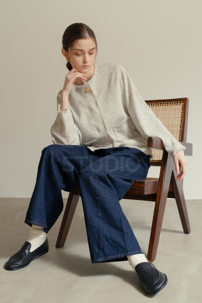 白壁モルタルグレー壁にピエールジャンヌレの椅子に腰かけ、デニムの質感を自然な動きをとらえたモデルによるECアパレルのモデル撮影写真