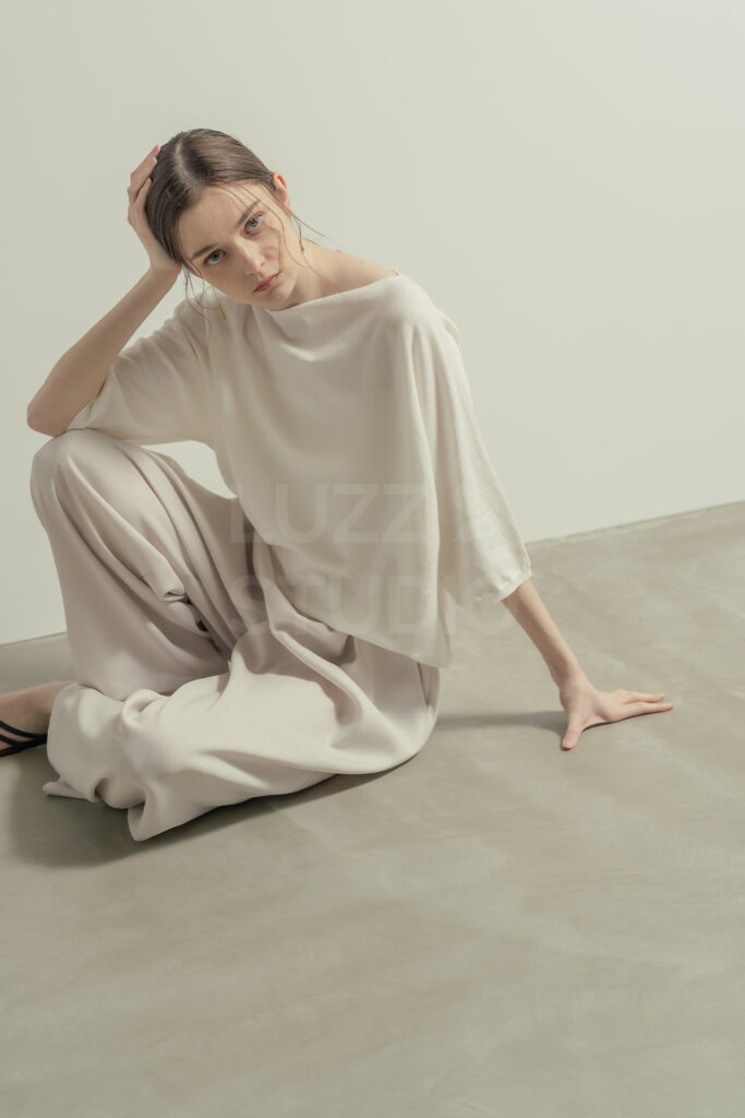 白壁モルタルグレー壁のシチュエーションで座り込むモデルをとらえたＥＣアパレルのモデル撮影写真